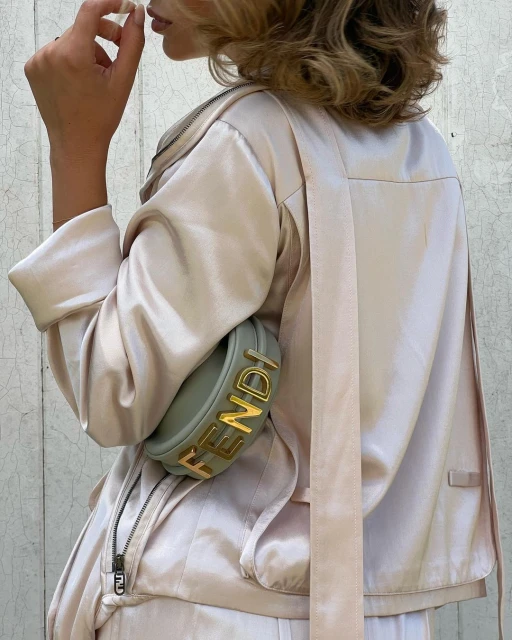 Fashionably dressed woman in a satin jacket with a Fendi handbag over her shoulder, showcasing contemporary style and luxury accessories.