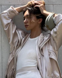 Content creator Bella Varelis posing against a textured wall in a satin jacket and white ribbed top