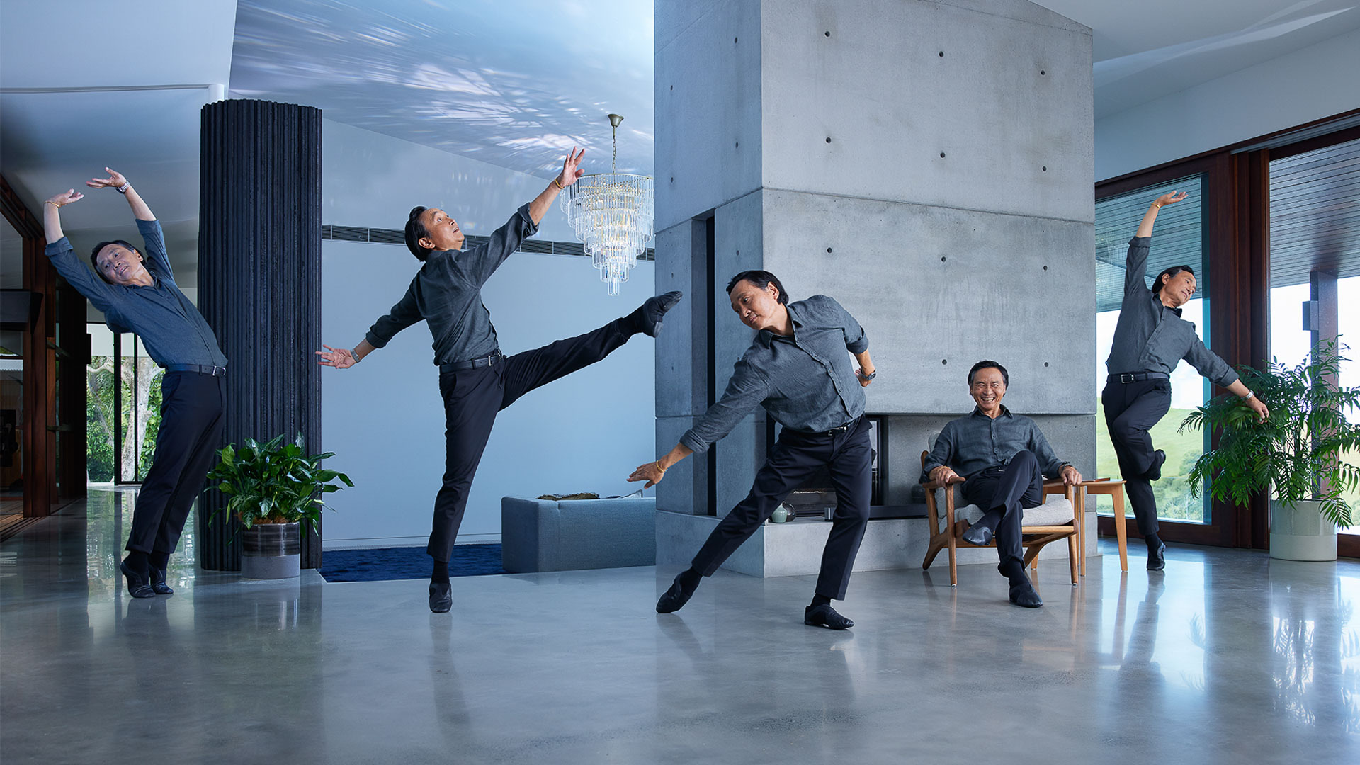 Multiple exposures capture an Asian adult male in an interior with modern decor and architecture, dressed in black pants and grey shirt, dancing.