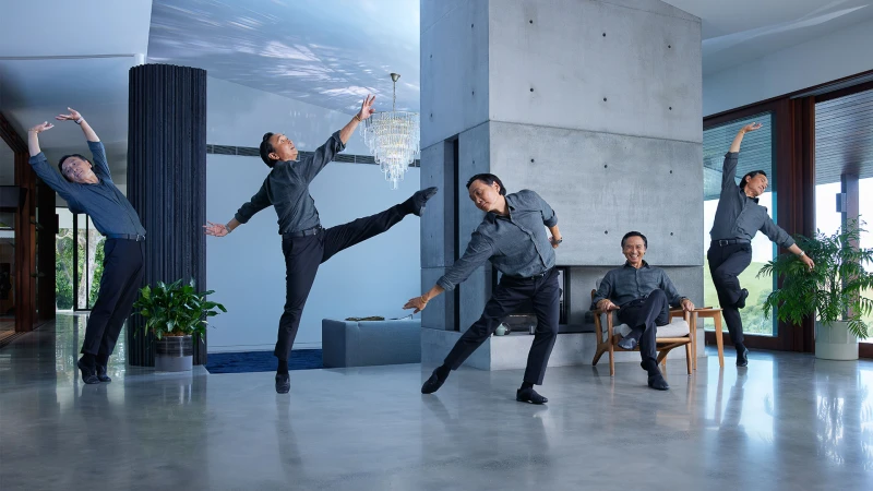 Multiple exposures capture an Asian adult male in an interior with modern decor and architecture, dressed in black pants and grey shirt, dancing.