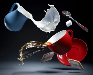 Floating red teacup pouring tea, blue jug splashing milk, sugar cubes, spoon, and biscuits against a dark background