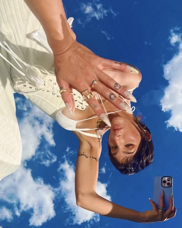 Low-angle shot of woman wearing rings and holding a smartphone against bright blue sky