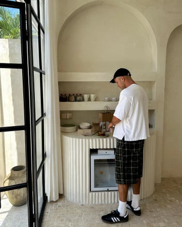 Adult male in casual clothes prepares food at a counter in a modern interior with natural light and neutral tones in a lifestyle setting.