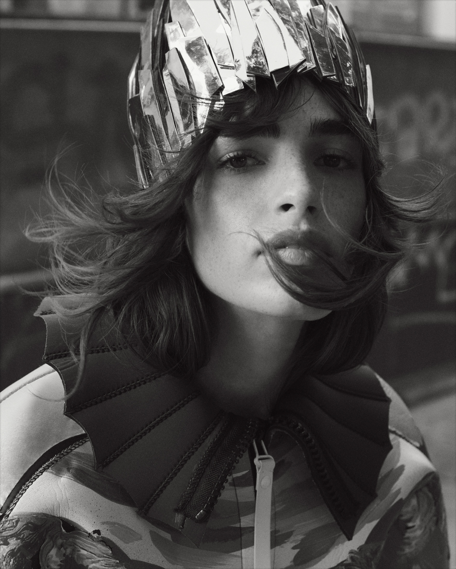 Close-up black and white portrait of a woman wearing a metallic headpiece and jacket with large collar, captured at eye-level.