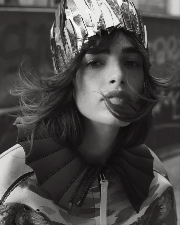 Close-up black and white portrait of a woman wearing a metallic headpiece and jacket with large collar, captured at eye-level.
