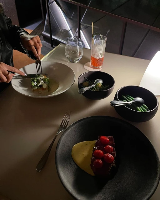 Person using utensils to eat a meal with multiple dishes, including meat with cherries, served on a beige table in a restaurant.