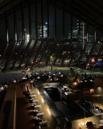 Indoor dining at a restaurant with a bar and a night cityscape seen through large windows, creating an elegant and inviting atmosphere.