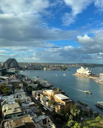 Scenic daytime cityscape showcasing Sydney Opera House, Harbour Bridge, and boats on the water under a partly cloudy sky.
