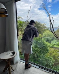 Man standing on a balcony leaning against a glass railing overlooking trees and water by Chad Cross