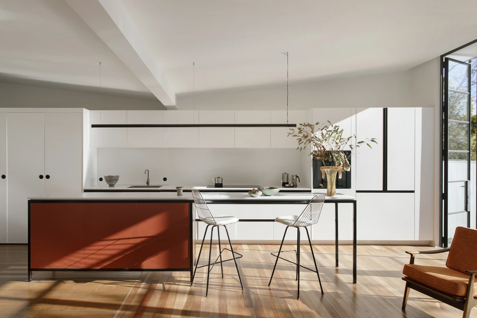 Bright, modern kitchen interior with white cabinets, an orange kitchen island, two stools, hardwood floor, and natural light from a window.