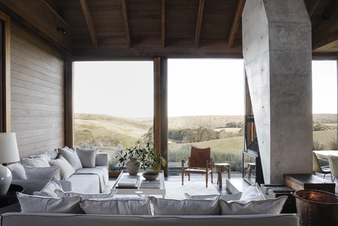 Contemporary living room interior features neutral sofas, a concrete fireplace, a leather chair, and a landscape view through large windows.
