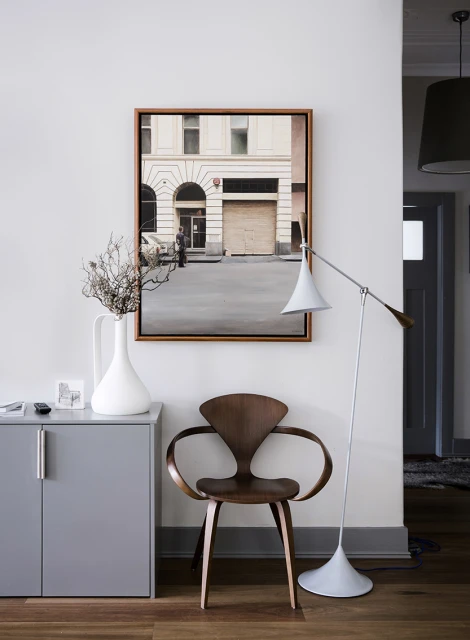Interior design featuring a wood chair and a floor lamp next to a grey cabinet, with artwork hanging on a white wall.