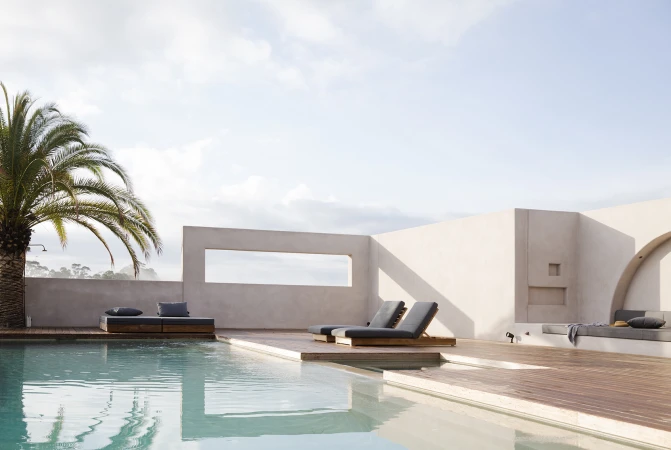 Modern outdoor pool area with wooden decking, sun loungers, and a palm tree under an overcast sky, photographed in Sydney.