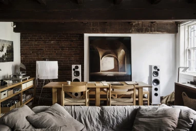 Interior shot of a living room with wooden dining table, chairs, large framed artwork, and exposed brick wall by Chris Warnes