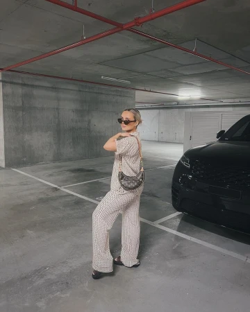 Stylish adult female poses in patterned pajama set in a parking garage with a black SUV and handbag. Cool, fashionable. 