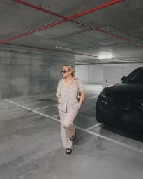 Woman in patterned two-piece shirt and trousers standing in a concrete parking garage next to a black SUV