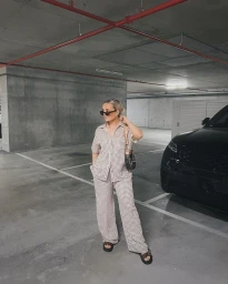 Woman in patterned short-sleeve shirt and matching trousers standing in a concrete parking garage near a black car.
