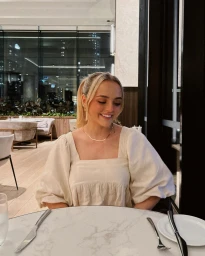 Blonde woman wearing a cream square-neck top seated at a round marble table in a restaurant by Conagh Kathleen