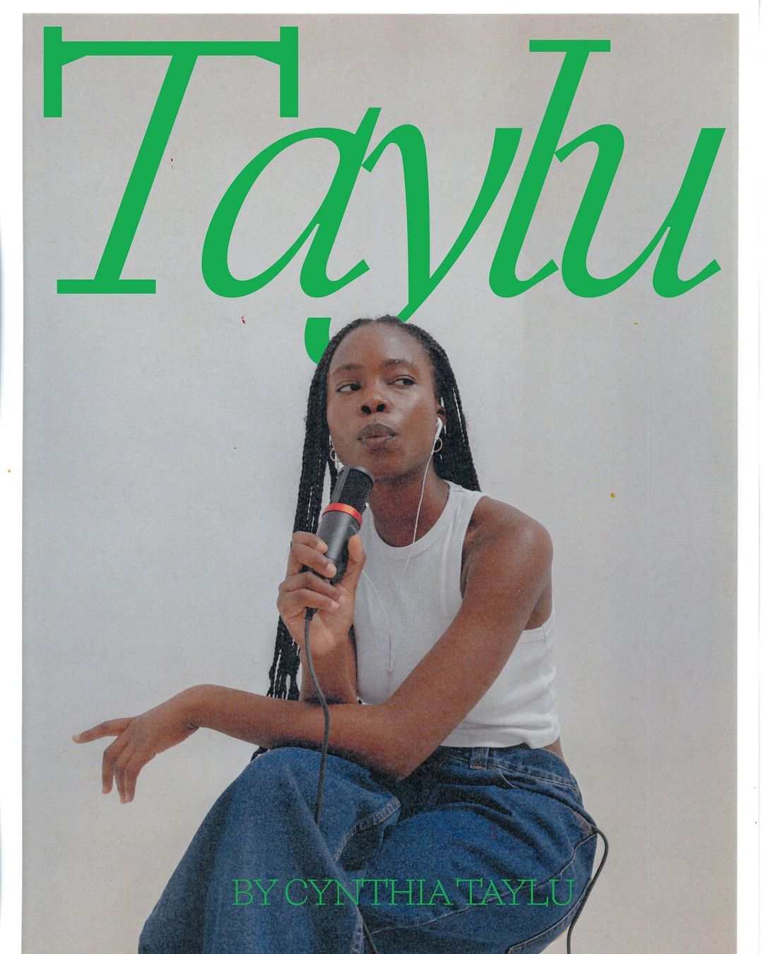Woman with braids and denim pants holds a microphone and appears to be singing in front of a white background with green text.
