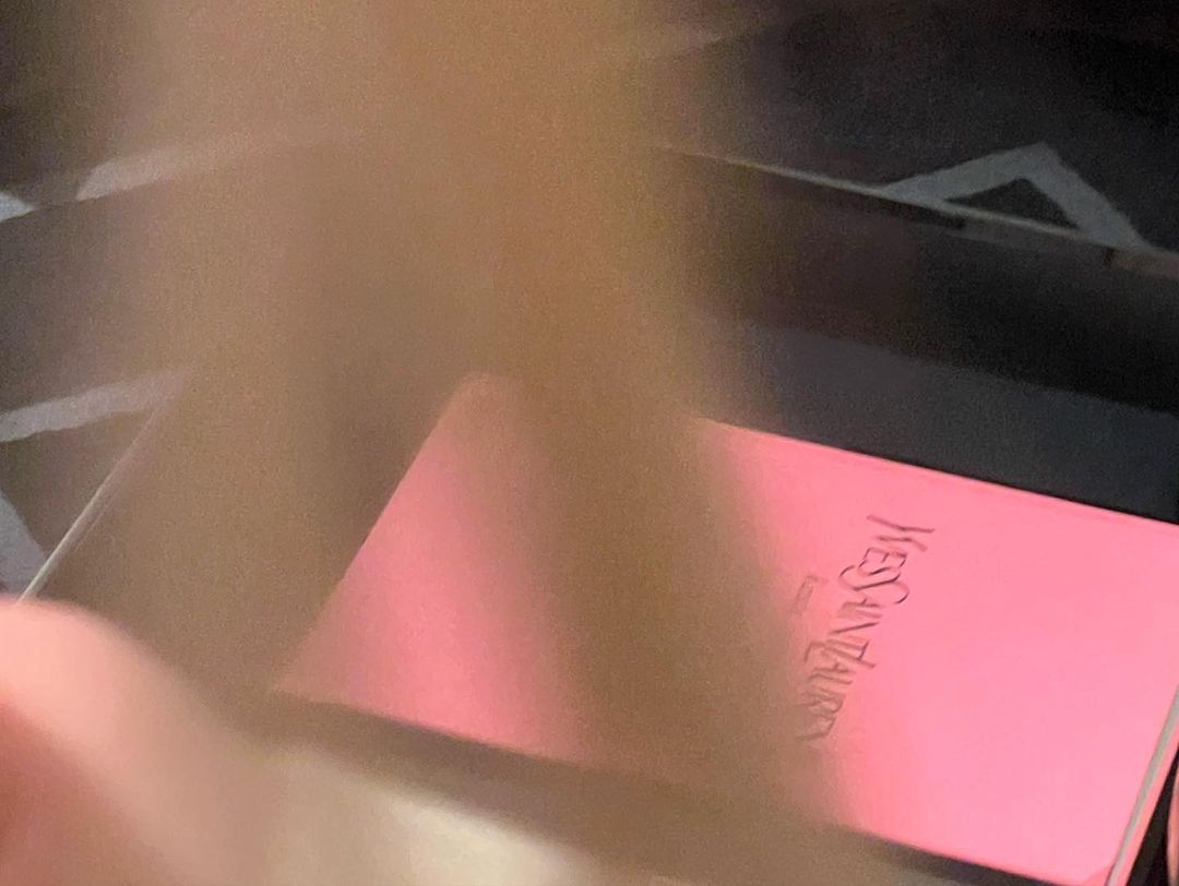 Close-up of a pink YSL box with its logo and Paris inscription, set against a dark background, showcasing beauty product packaging.