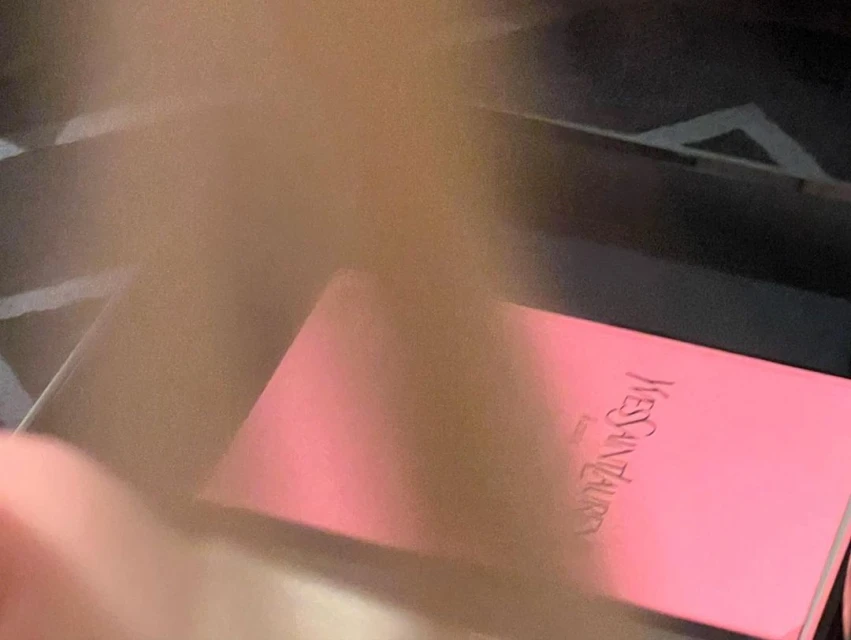 Close-up of a pink YSL box with its logo and Paris inscription, set against a dark background, showcasing beauty product packaging.