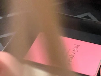 Motion-blurred hand passing over a pink Yves Saint Laurent product box inside a dark container.