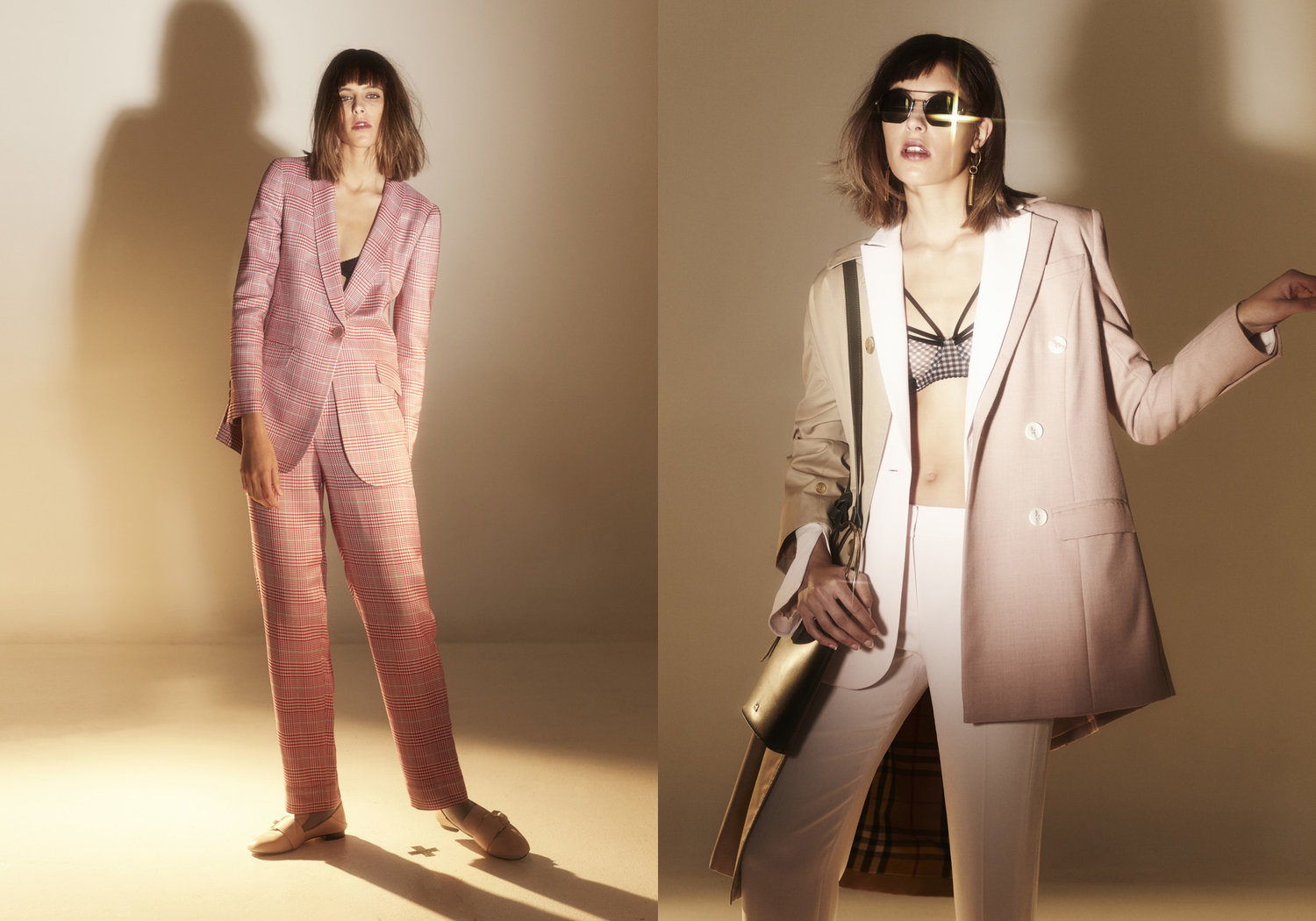 Two adult women in blazers and pants posing in a photo studio with warm lighting, showcasing fashion and style trends in an editorial shot.