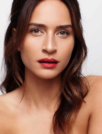 Close-up portrait of a woman with vibrant red lipstick and highlighted brown hair against a white background