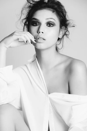 Black and white portrait of a woman with dark smokey eye makeup wearing an off the shoulder white button down shirt