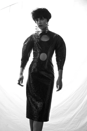 Monochrome portrait of a woman wearing a patterned cut-out dress with statement earrings against a plain white background