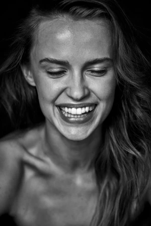 Close-up monochrome portrait of a smiling woman with tousled hair against a dark background, captured by Andrea Black in Sydney.