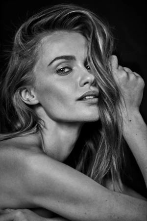 Close-up black and white portrait of a woman with tousled hair framing her face against a dark background.
