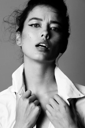 Black and white close-up portrait of a woman in a white collared shirt with winged eyeliner, makeup by Andrea Black