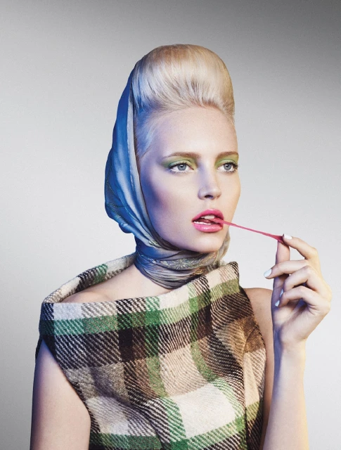 Blonde woman with high hair and headscarf wearing plaid shawl, blowing bubblegum. Beauty and fashion headshot, studio lighting.