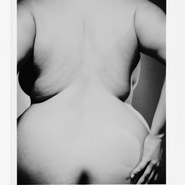 Monochrome portrait of a woman's back and hand, emphasizing curves and texture in a photo studio setting with soft lighting.