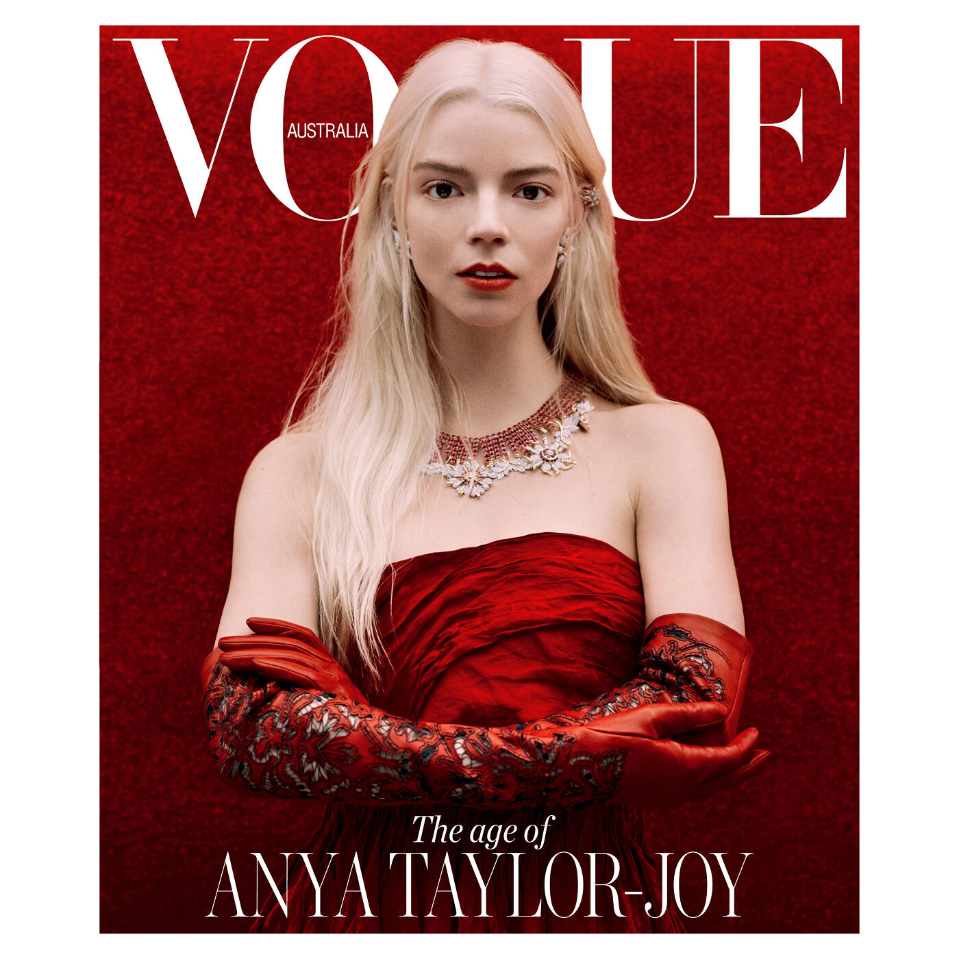 Anya Taylor-Joy on the cover of Vogue Australia, posing in a strapless red dress with matching gloves and an ornate necklace on a red background.