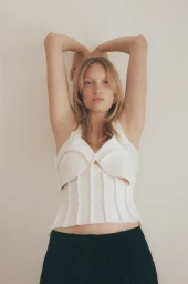 Portrait of a blonde woman wearing a white corset top and black skirt against a plain wall in Sydney by Jess Ruby James.