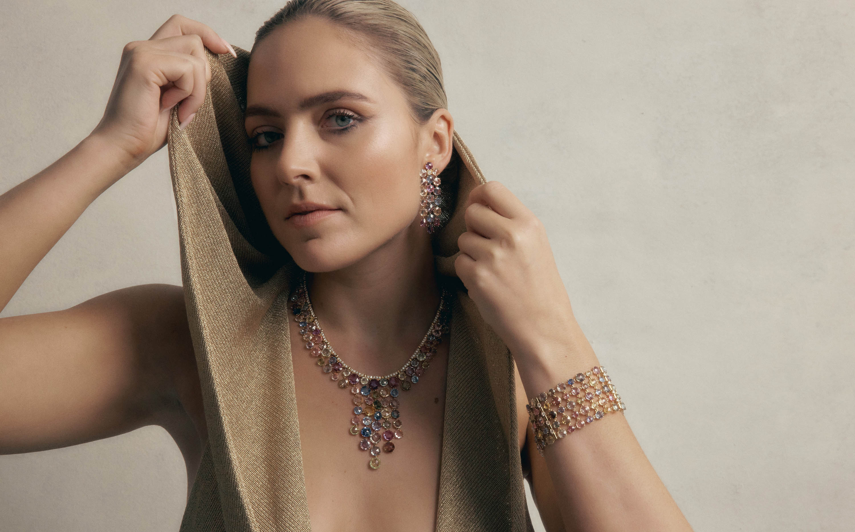 Woman poses indoors wearing multicolored teardrop-shaped gemstone jewelry set including a necklace, bracelet, and dangling earrings.