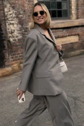 Woman wearing round sunglasses and a grey oversized blazer walking on a street