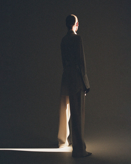 Fashionable adult poses in elegant suit and pants, standing in dramatic spotlit indoor studio. Style and sophistication in portrait.
