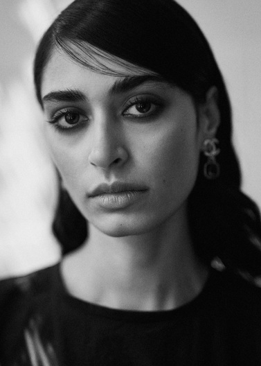 Monochrome portrait of a woman with dark hair and striking makeup, featuring Chanel earrings and a serious expression. Black and white aesthetic.