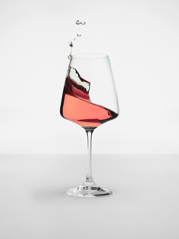 Elegant clear wine glass with splashing pink rose wine on a white table against a plain white backdrop in a minimalist still life.