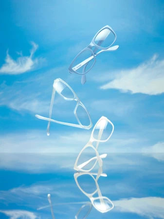 Three pairs of white framed glasses levitating against a bright blue sky with wispy clouds and reflective surface