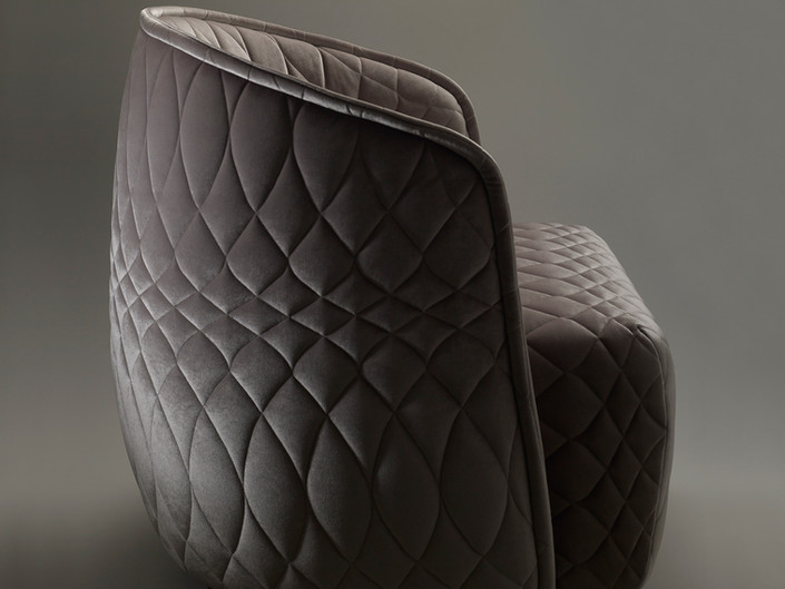 Close-up of a grey quilted armchair with a modern design. The quilted pattern is diamond-shaped, creating a plush, textured appearance.