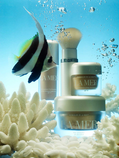 La Mer beauty products displayed with a moorish idol fish and coral against a blue underwater backdrop with rising bubbles.