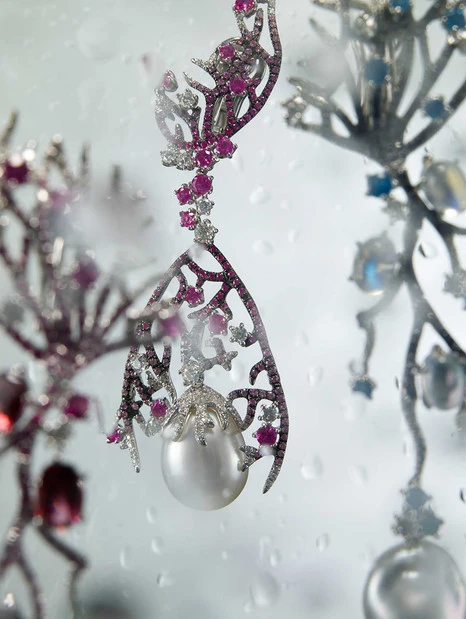 Close-up of ornate silver earrings with pink and white gems and dangling pearl drops, photographed in a clean, minimalist style.