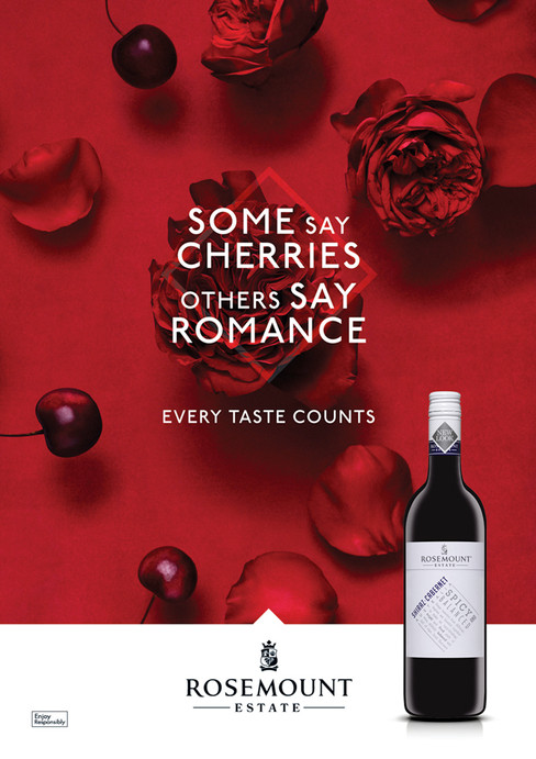 Still life with a bottle of Rosemount wine, cherries, and red rose petals against a red background in a studio food and beverage shot.