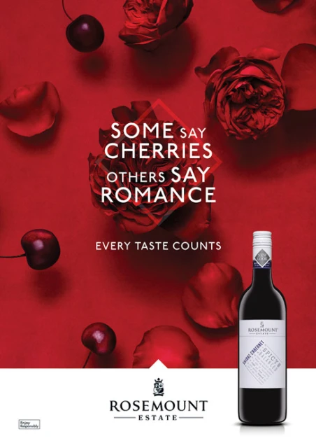 Still life with a bottle of Rosemount wine, cherries, and red rose petals against a red background in a studio food and beverage shot.