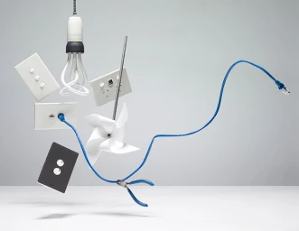 Floating electrical hardware including lightbulb wall switches pinwheel and blue ethernet cable against a grey background