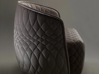 Close-up of a modern armchair upholstered in taupe quilted velvet fabric against a dark studio background
